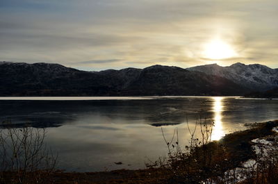 The shot of the sun which is going to take a rest in clouds behind the mountains on the bank of mountain lake