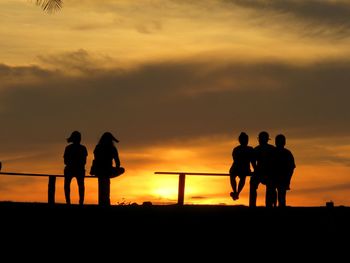 Silhouette friends standing on land against sky during sunset