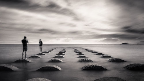 Men standing on beach against sky during sunset