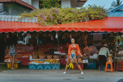 A young girl in red near a fruit stand on the street