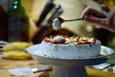 Person prepairing cake with whipped cream on table