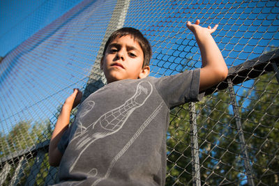 Portrait of boy standing against chainlink fence