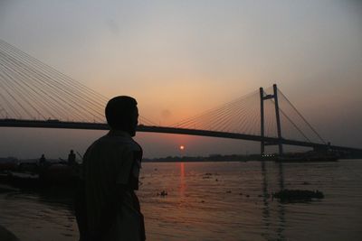 Silhouette of man standing on bridge at sunset