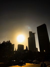 City street by buildings against sky during sunset