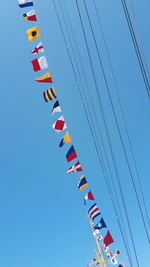 Low angle view of flags hanging against clear blue sky