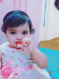 Portrait of cute baby girl sitting on bed at home