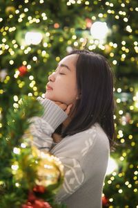 Portrait of young woman looking away against christmas tree