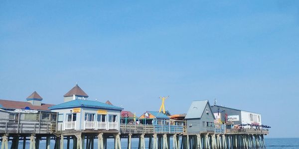 Stilt houses on sea against buildings against clear blue sky