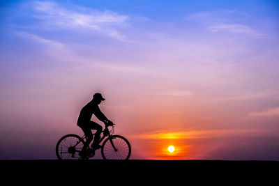 Silhouette man riding bicycle against sky during sunset