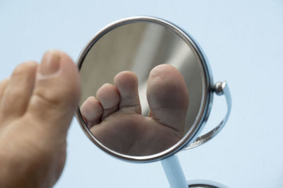 Low section of man by mirror against blue background