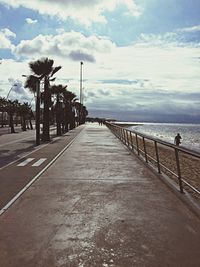 Walkway leading towards sea against cloudy sky