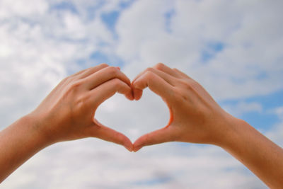 Midsection of woman holding heart shape against sky