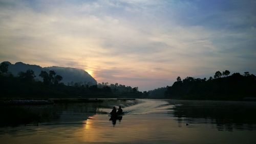 Silhouette man on lake against sky during sunset