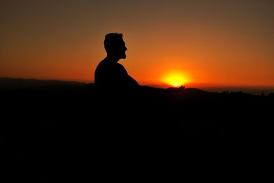 Silhouette man standing on landscape against sky during sunset