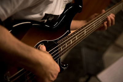 Midsection of man playing guitar while sitting indoors