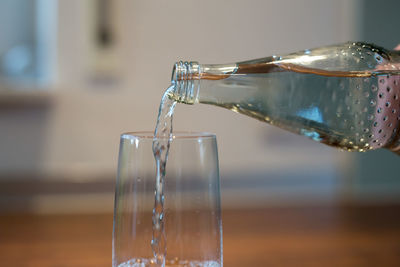 Bottle pouring water in glass on table