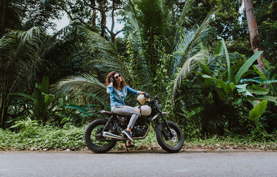 Woman sitting on motor cycle near forest