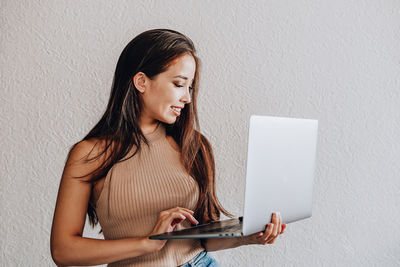 Young woman using mobile phone against wall