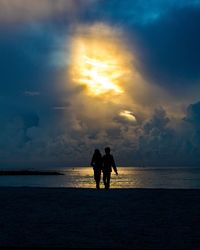 Silhouette couple on beach against sky during sunset