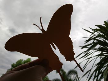 Low angle view of hand holding leaf against sky