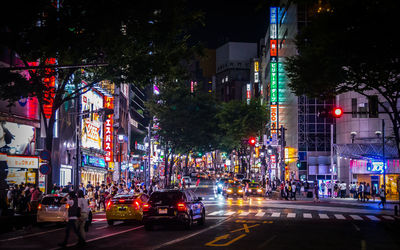 People and cars on street at illuminated shibuya ward