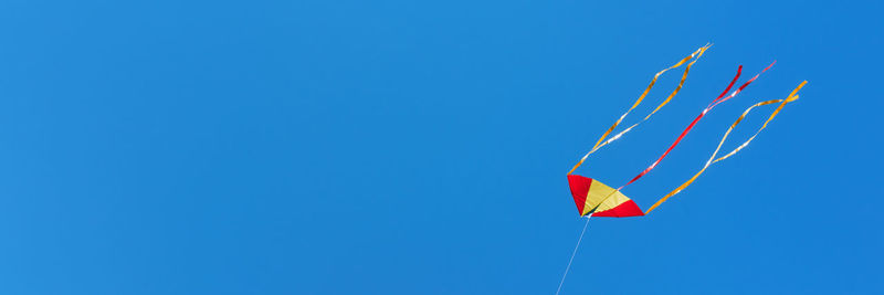 Red yellow kite fly high in blue cloudless sky. soft focus, copy space, banner format