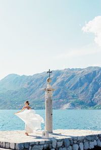 Rear view of woman standing by sea against sky