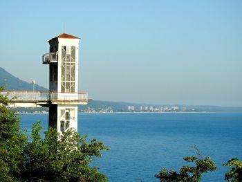 Lighthouse by sea against clear sky