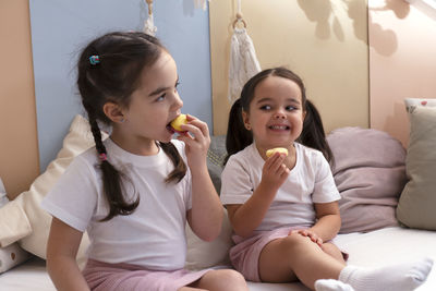 Two little cute siblings girls sitting on the bed eating cake macaroon. happy moment concept.