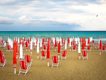 Closed parasols with deck chairs at beach against sky