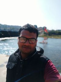 Portrait of young man with eyeglasses against sky