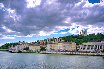 Bridge over river by buildings in city against sky