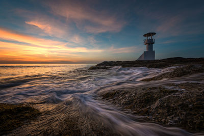 Lighthouse by sea against sky during sunset