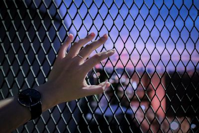 Midsection of woman touching chainlink fence