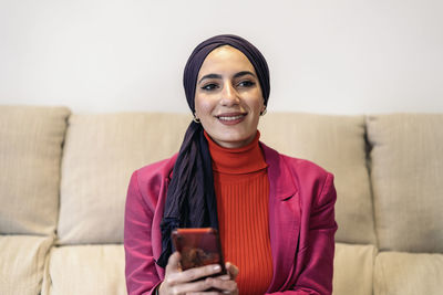 Young woman using phone while sitting on sofa at home