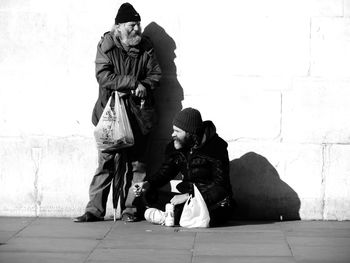 Senior beggars on street against wall during sunny day