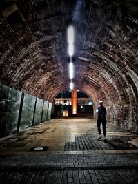 Rear view of man walking in illuminated tunnel