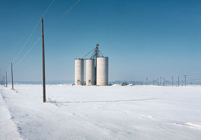 Three agriculural silos photographed on a snow covered open field on a cold winter's day.