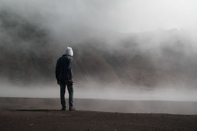 Rear view of man standing against mountain during foggy weather