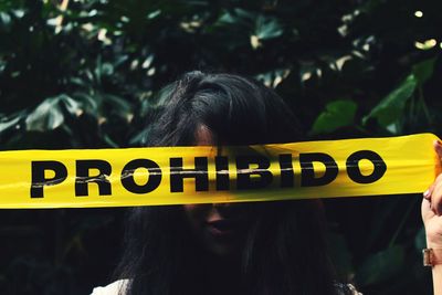 Close-up of woman holding yellow tape with text