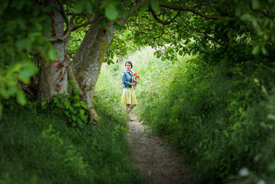 Woman in yellow dress gathering poppy and wildflowers, walking in summer meadow