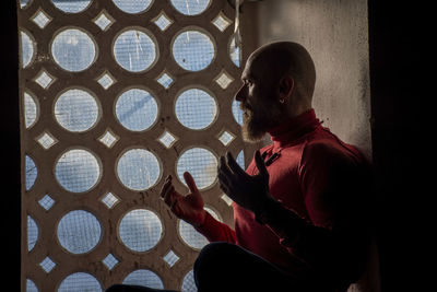 Side view of man gesturing while sitting nu window