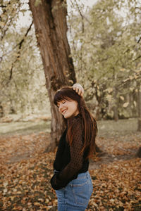 Portrait of smiling young woman standing on tree trunk