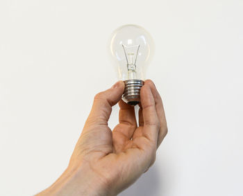 Close-up of hand holding light bulb against white background