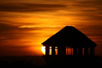 Silhouette built structure against orange sky