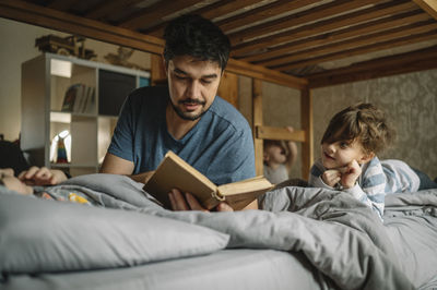 Father reads book to his sons on bed at home