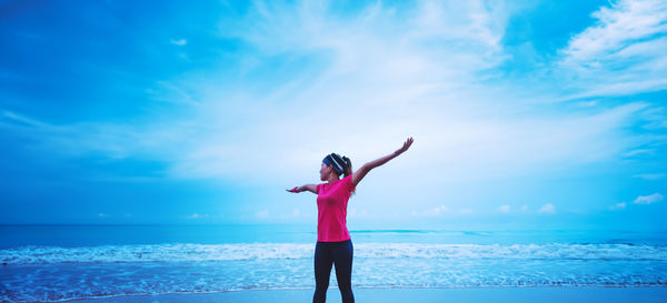 Rear view of woman with arms raised standing at beach against sky