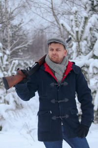 Young man holding rifle while standing outdoors during winter