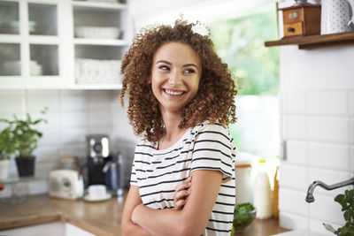 Smiling teenage girl with arms crossed standing in kitchen at home