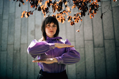 Portrait of young woman gesturing equal sign while standing against wall